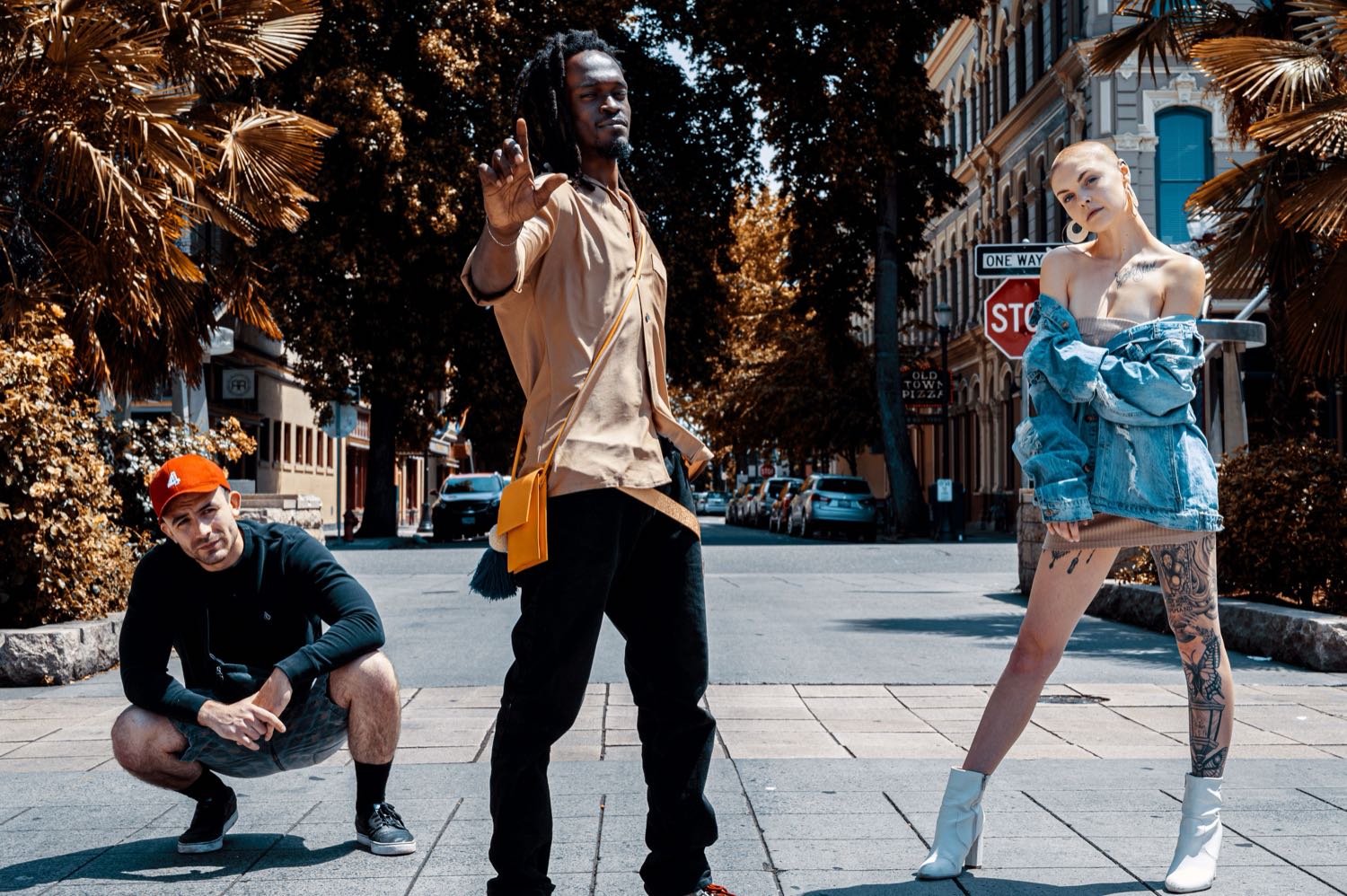 Three people in distinctive street-style fashion posing on a sunny city street